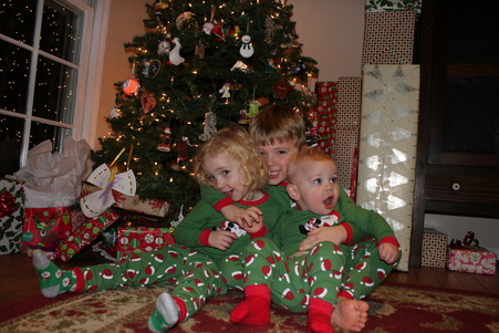 Three children in matching pajamas in front of a Christmas tree.